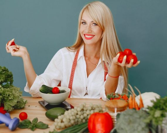 Healthy lifestyle concept with woman holding tomatoes and surrounded by fresh vegetables in a studio setting.