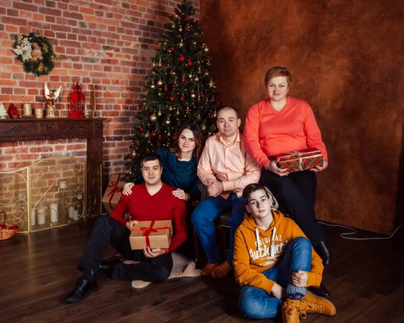A family posing with Christmas gifts by a decorated tree indoors, exuding holiday warmth.