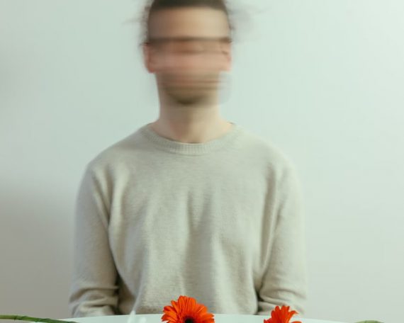 Blurred portrait of person with vibrant flowers on a white table.